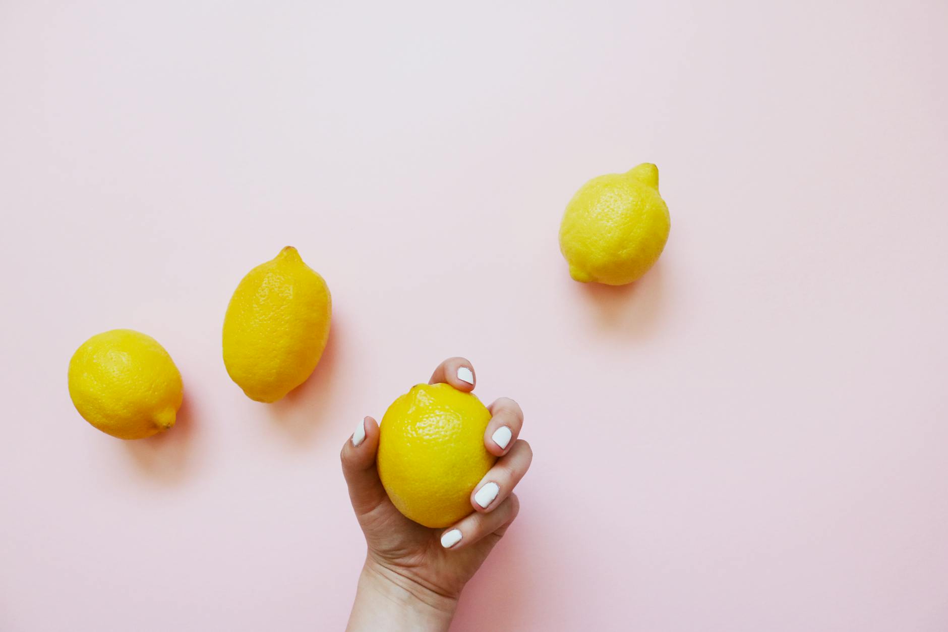 A hand holding a fresh lemon against a soft pink background, symbolizing vibrant pleasure potential