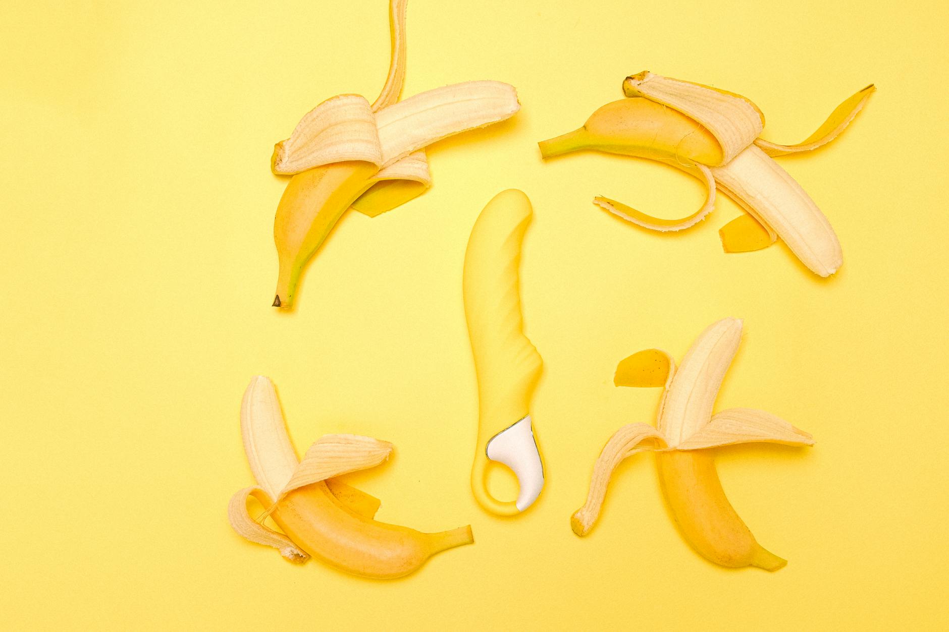Yellow silicone lemon vibrator surrounded by fresh citrus fruit and bananas on a bright yellow background