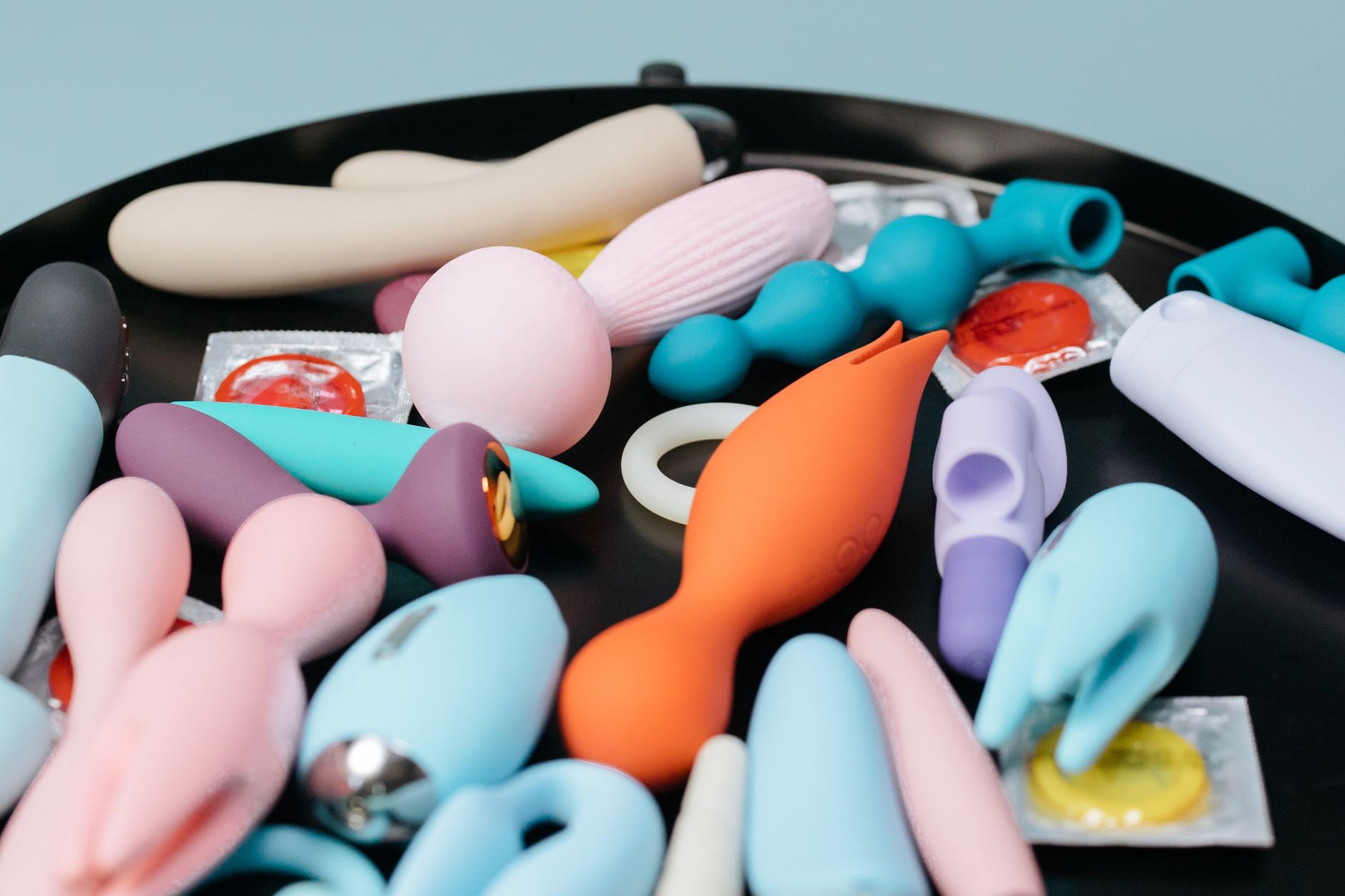 A collection of colorful vibrators on a black surface, including various shapes and designs for different sensations