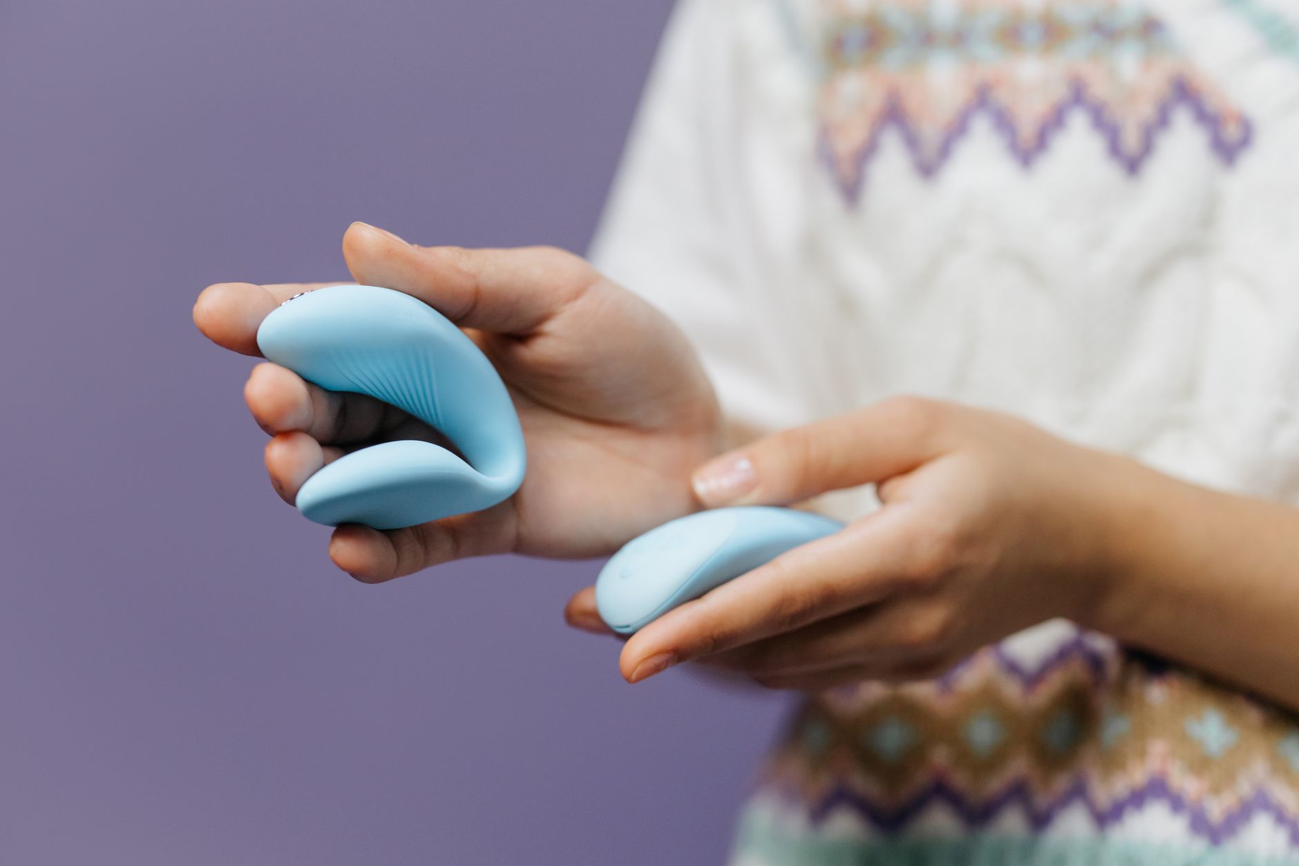 Hands gently holding a sleek blue vibrator against a purple background, symbolizing tender reconnection with pleasure