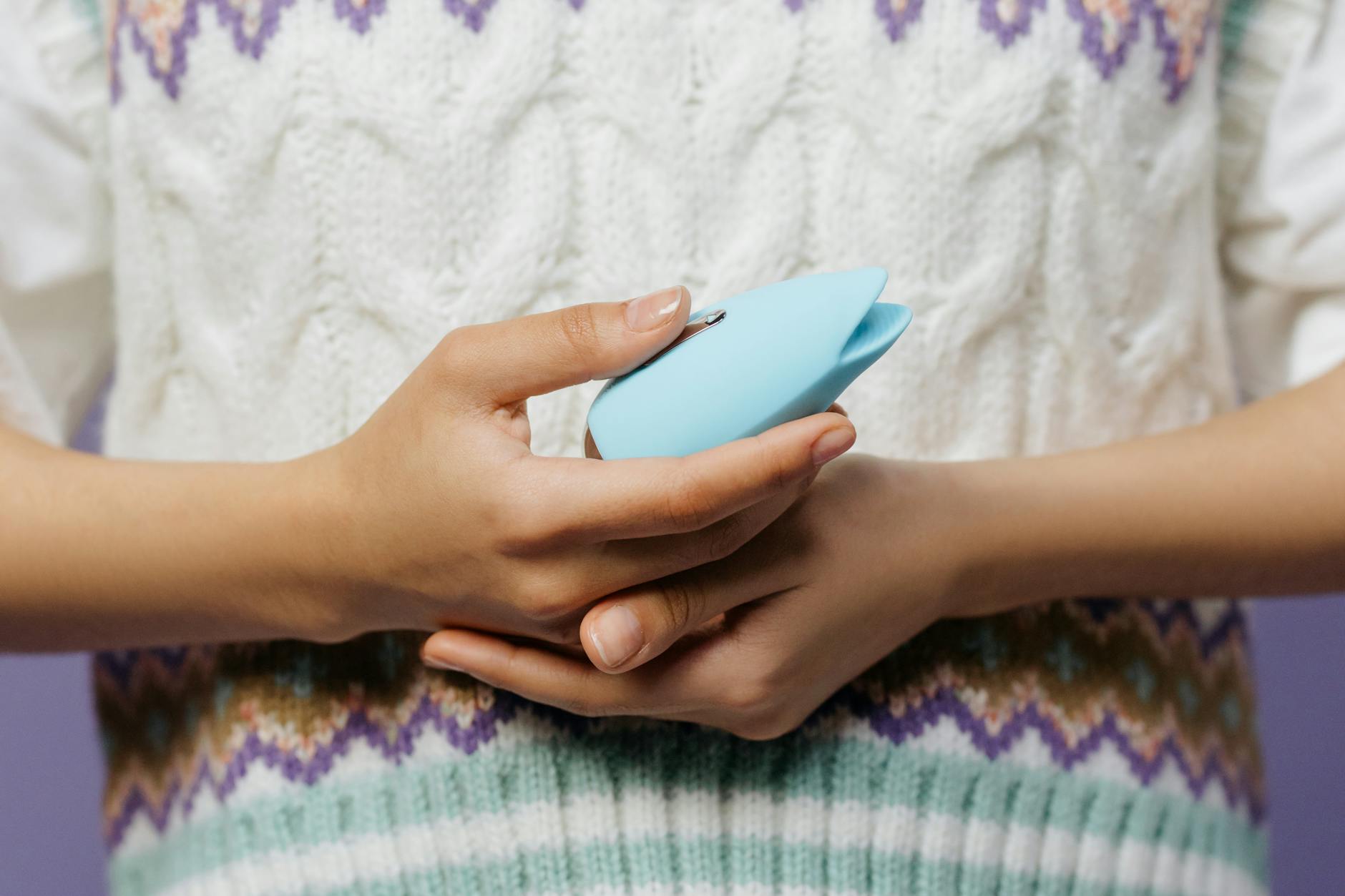 Nahaufnahme von Händen, die einen blauen persönlichen Massager gegen einen gestrickten Pullover halten