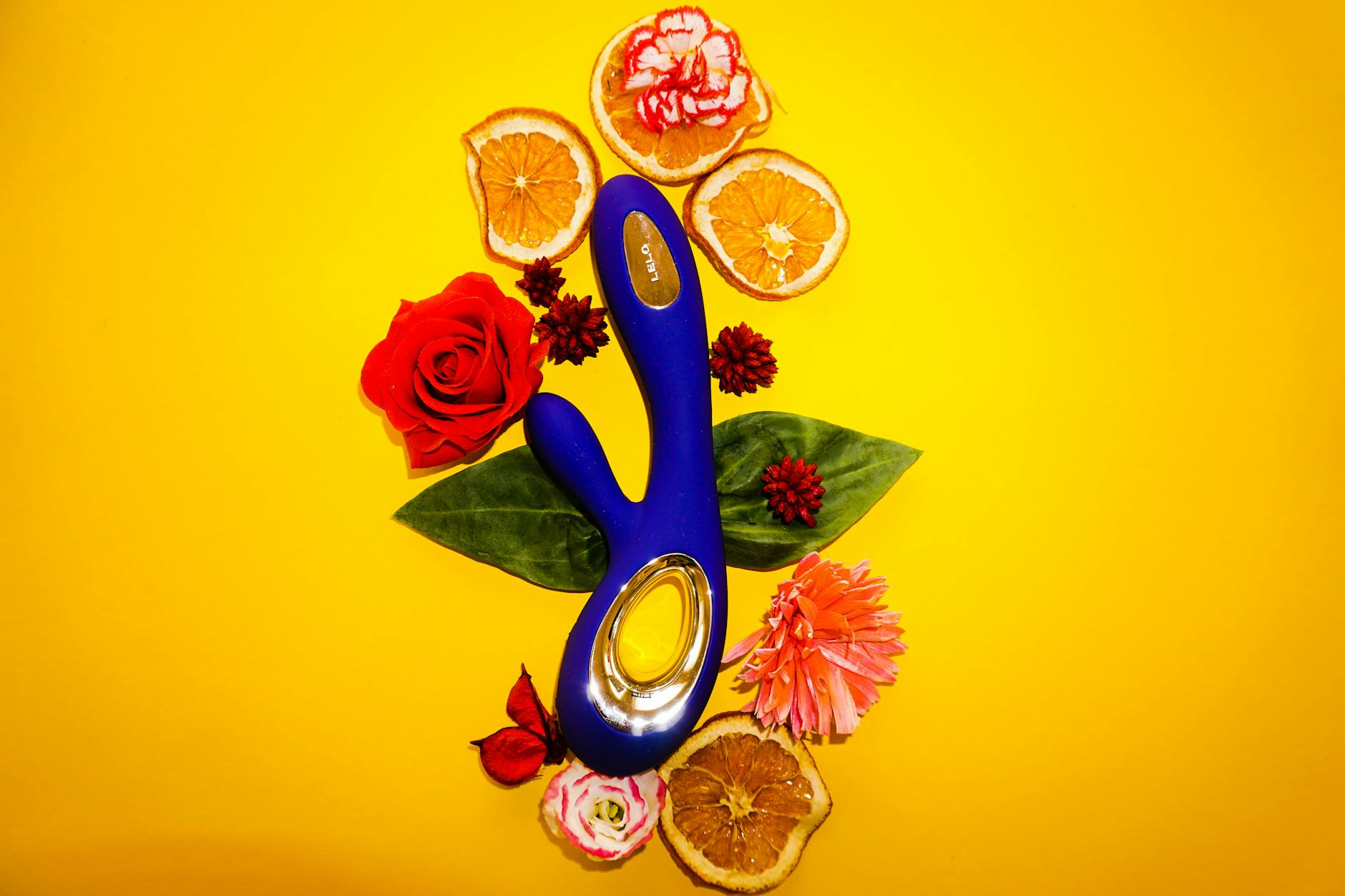 Blue lemon vibrator surrounded by bright flowers and citrus slices on yellow background